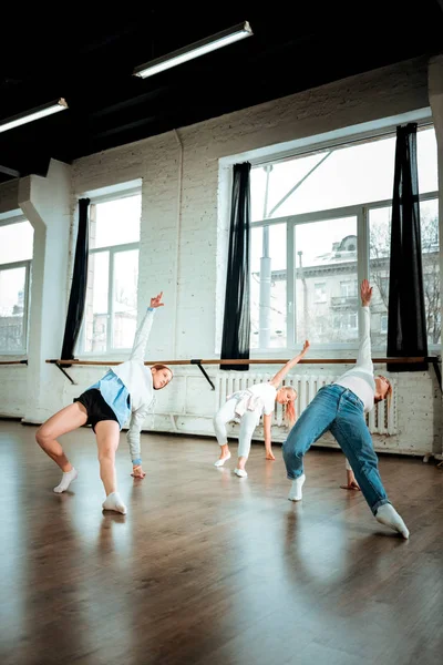 Roodharige dansleraar in spijkerbroek en haar studenten doen overkoepelende — Stockfoto