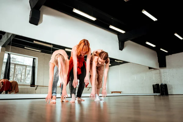Beautiful dance teacher with red hair and her students swinging their legs