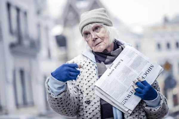 Sad senior woman selling newspapers to people on the street — Stock Photo, Image