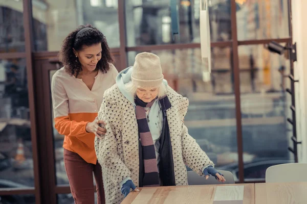 Joven alegre ayudando a una anciana a sentarse — Foto de Stock