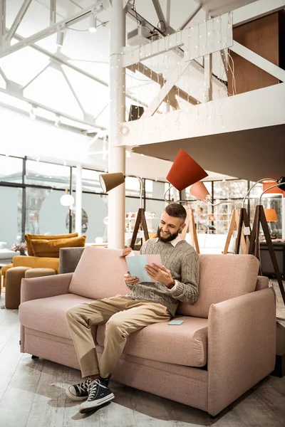 Lachender bärtiger Mann wartet auf gemütlichem Sofa auf seine Frau — Stockfoto