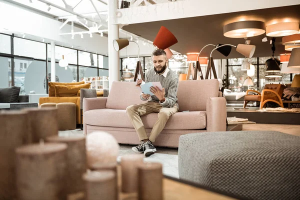 Curious bearded man observing catalog with variants of furniture — Stock Photo, Image