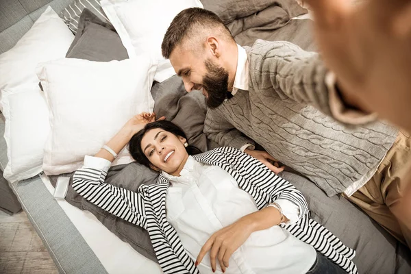 Attraktive dunkelhaarige Frau entspannt sich auf dem Bett, während ihr Mann ein Foto macht — Stockfoto