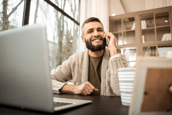 Mörkhårig man med brett leende bär smartphone och diskutera — Stockfoto