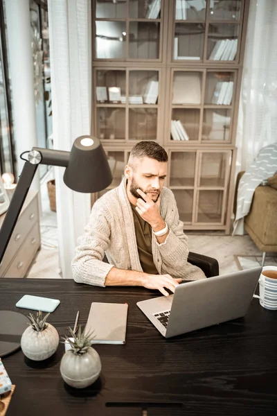 Doordachte dark-haired mens zijn baard wrijven terwijl u op het scherm — Stockfoto