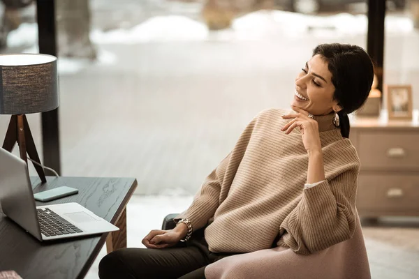 Laughing appealing woman in beige warm sweater watching video — Stock Photo, Image