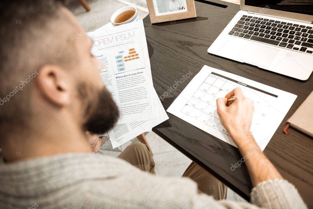 Responsible well-organized man filling up calendar with affairs