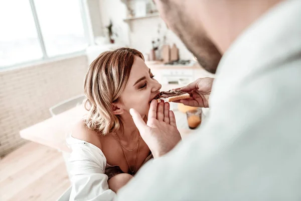 Jonge langharige mooie vrouw in een wit overhemd eten boterham met chocopasta — Stockfoto