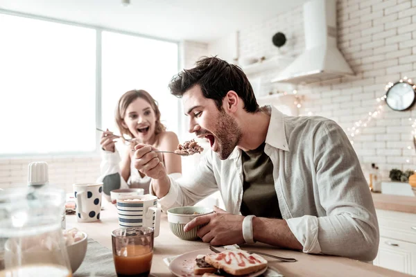 Barbudo guapo hombre positivo en una camisa blanca comiendo ensalada para el desayuno — Foto de Stock