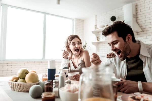 Γενειοφόρος όμορφος θετικός άνθρωπος σε ένα λευκό πουκάμισο τρώει έχοντας πρωινό με τη σύζυγό του — Φωτογραφία Αρχείου