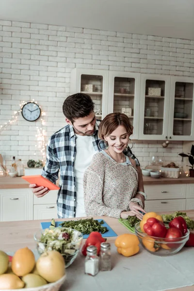 Junge strahlende hübsche Frau mit großen Ohrringen und ihrem Mann, der gemeinsam Grünzeug schneidet — Stockfoto