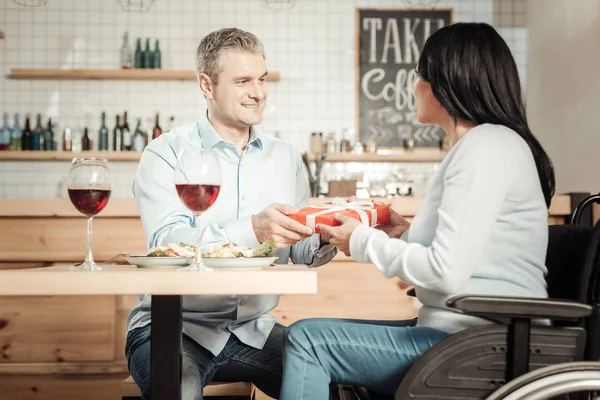 Mujer agradable en silla de ruedas presentando regalo al hombre — Foto de Stock