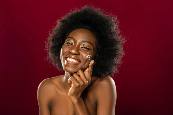 Encantada mujer afroamericana poniéndose crema en la mejilla — Foto de Stock