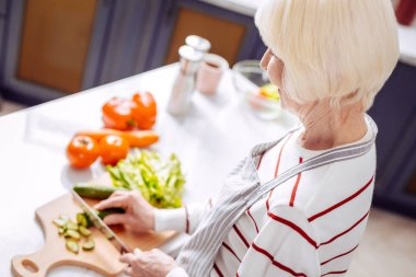 Keskin bıçak ve kesim salatalık tutan sakin üst düzey kadın