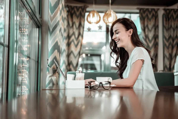 Wesoła osoba płci żeńskiej, siedząc w pozycji pół w kawiarni — Zdjęcie stockowe