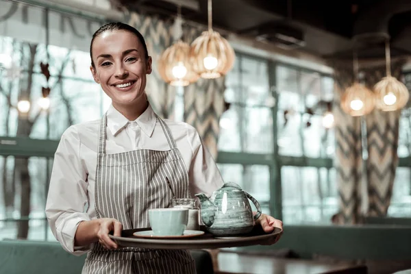 Verheugd brunette meisje houden van thee set op houder — Stockfoto