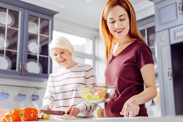 Mulher sênior cortando legumes enquanto cozinha salada com sua filha — Fotografia de Stock