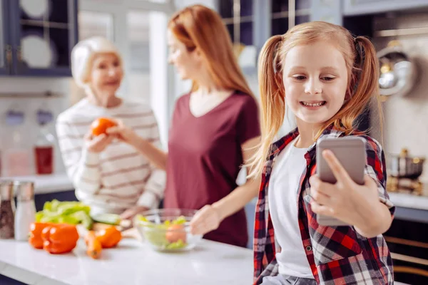 Emocional chica sonriendo y tomando selfies con sus parientes ocupados — Foto de Stock