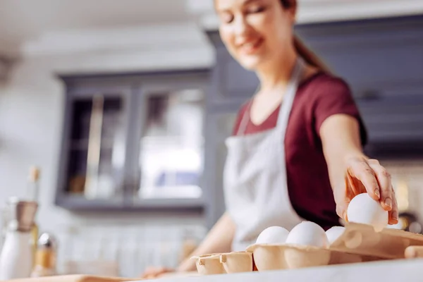 Sonriente jovencita sacando la mano y sacando un huevo de la caja — Foto de Stock