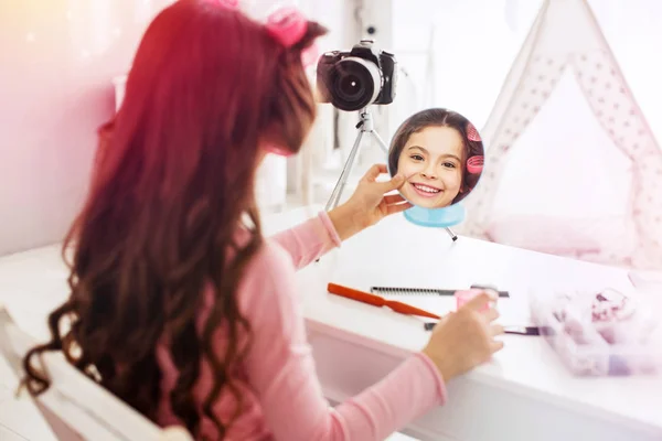Cute beaming dark-eyed girl smiling broadly looking into mirror curling her hair — Stock Photo, Image