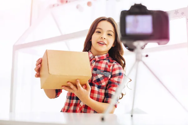 Emocionado linda chica con el pelo ondulado largo diciendo acerca de su caja de regalo durante la filmación de vídeo — Foto de Stock