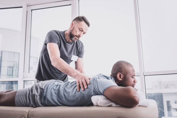 Внимательный бородатый мужчина делает массаж своему пациенту
