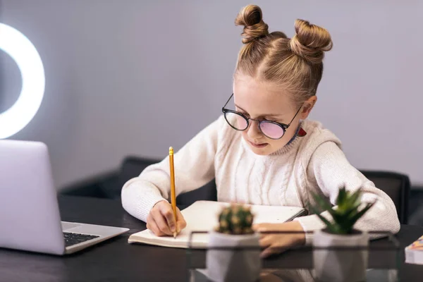 Cute blue-eyed long-haired girl in a white sweater writing something in a notebook — Stock Photo, Image