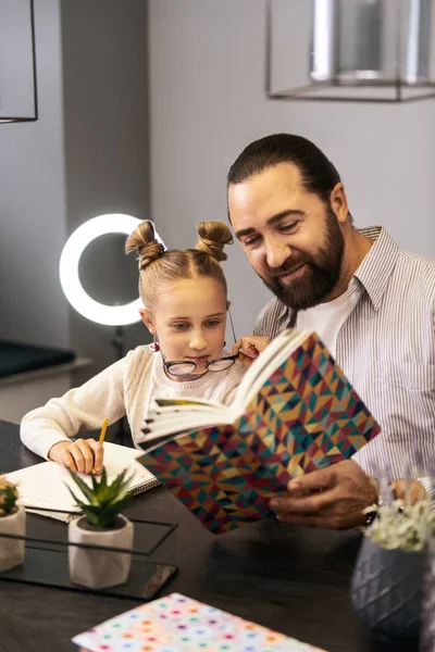 Profesor barbudo de cabello oscuro con una camisa a rayas leyendo un libro con su alumno — Foto de Stock
