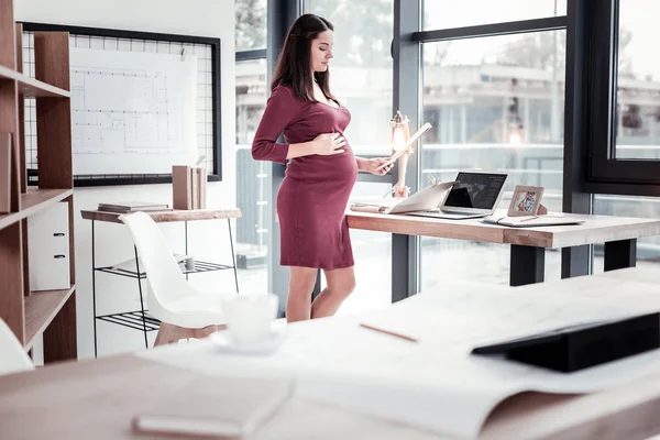 Pregnant sentimental woman in dark red dress reading congratulation letter — Stock Photo, Image