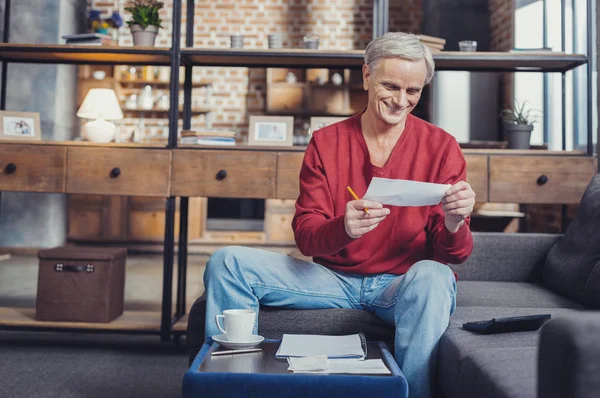 Vrolijk gepensioneerde glimlachen tijdens het kijken naar de rekeningen in zijn handen — Stockfoto