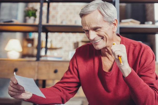 Homme âgé émotionnel souriant et regardant les factures dans sa main — Photo