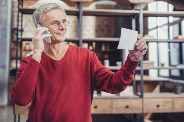 Hombre de edad inteligente mirando el documento importante mientras habla por teléfono — Foto de Stock