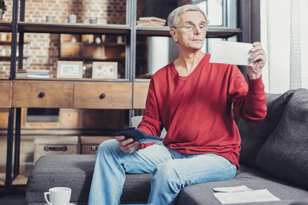 Внимательный пенсионер тщательно проверяет счета, находясь дома — стоковое фото