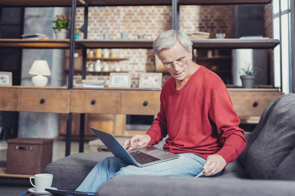 Emeryt nowoczesne gospodarstwa laptopa siedząc na kanapie — Zdjęcie stockowe