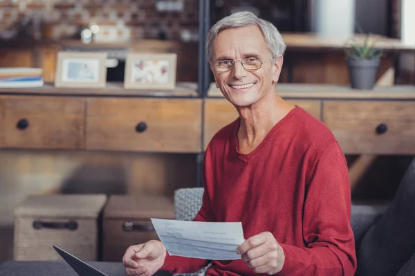 Pensionista positivo sintiéndose satisfecho con sus facturas y sonriendo — Foto de Stock
