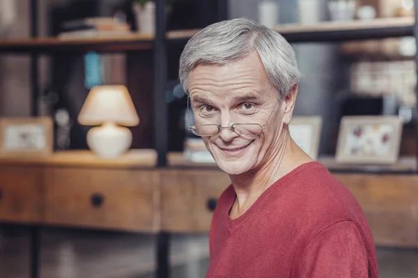 Alter Mann sieht neugierig aus, während er allein sitzt und lächelt — Stockfoto