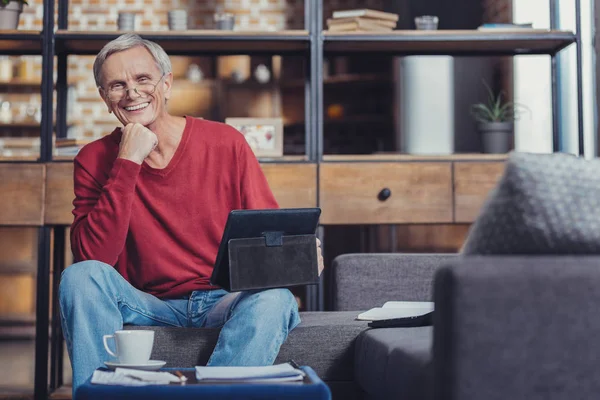 Aposentado positivo sorrindo enquanto sentado com um comprimido — Fotografia de Stock