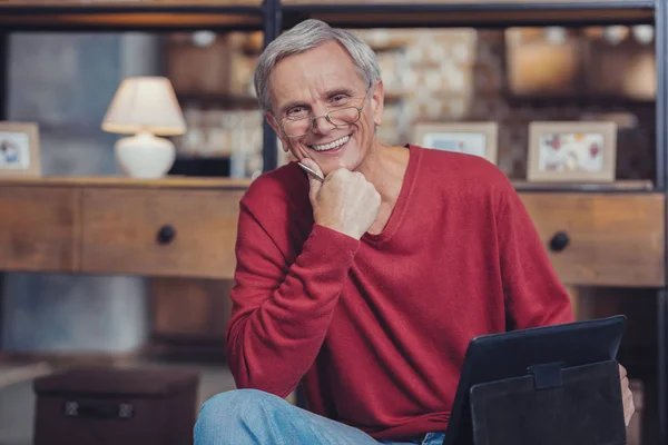 Homme âgé joyeux souriant tout en se relaxant avec sa tablette — Photo