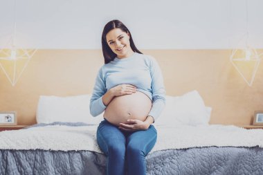 Evde olmak. Bebek karnı üzerinde eller giyerken pozitifliği ifade neşeli genç kadın