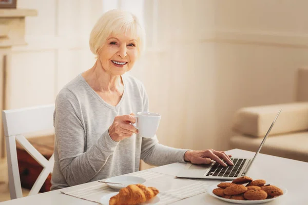 高齢者女性ビジネス レターを入力しながらビスケットを食べる — ストック写真