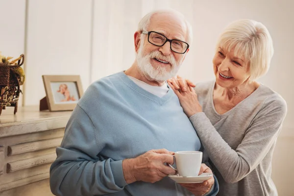 Uważny żona przynosząc niektóre gorącej herbaty dla jej uśmiechnięty mężczyzna — Zdjęcie stockowe