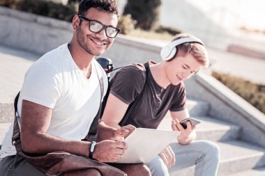 İyi bir ruh hali. Merdivenlerin üzerinde otururken diz ifade pozitifliği ve holding laptop neşeli genç adam