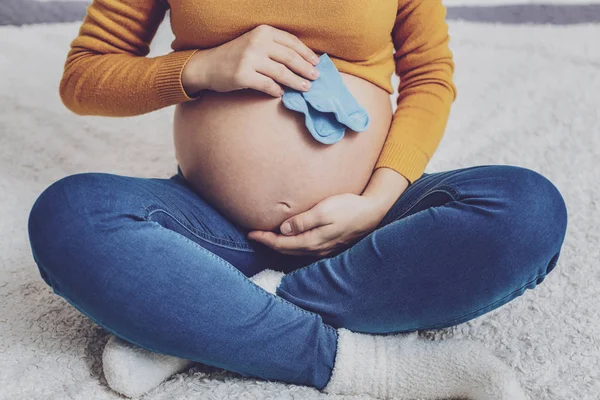Закрыть беременную женщину, которая держит синие носки — стоковое фото