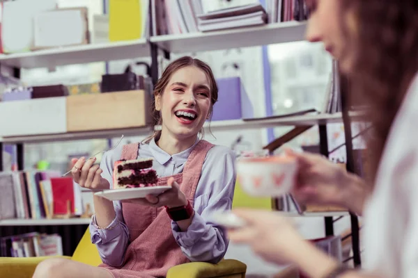 Riéndose mujer joven positiva llevando plato con pastel de esponja — Foto de Stock