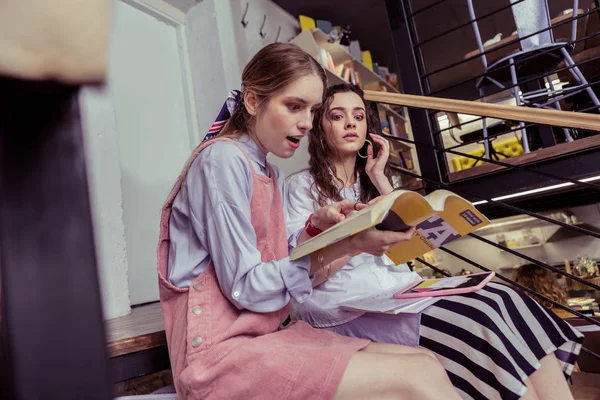 Shocked chicas de pelo claro mirando en el texto en el libro con la boca abierta — Foto de Stock