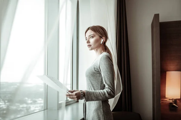 Mujer de cabello rubio con auriculares de pie cerca de la ventana — Foto de Stock