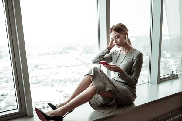 Mujer sentada en el alféizar de la ventana mientras lee noticias en smartphone — Foto de Stock