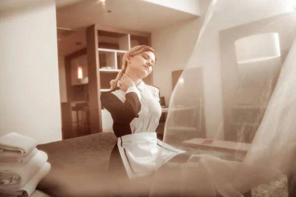 Young hotel maid enjoying light summer wind from the window — Stock Photo, Image