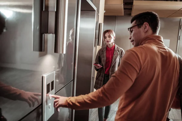 Calling the elevator. Dark-haired man wearing orange polo neck calling the elevator standing near his girlfriend