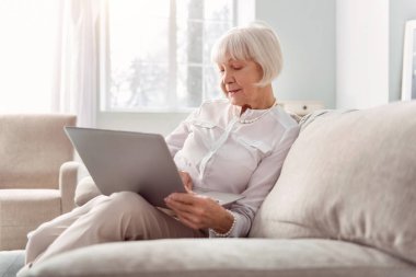 Oturma odasında dizüstü bilgisayarda çalışan yaşlı kadın